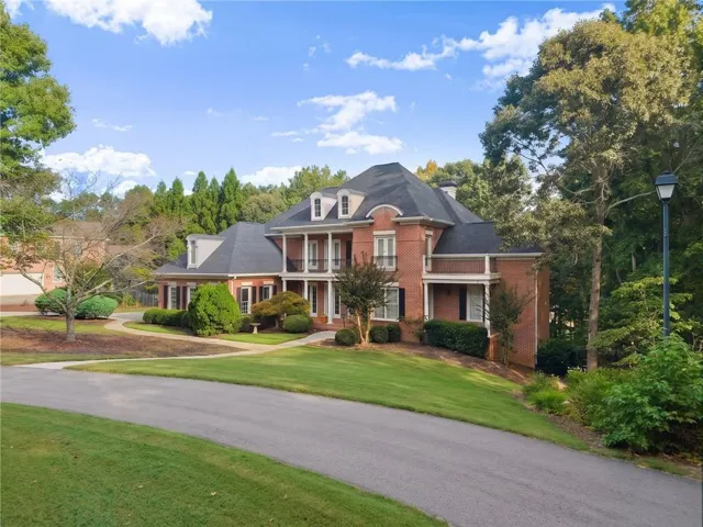 Brick exterior with multiple dormer windows, a circular driveway, mature trees, and a covered front entry. Virtually edited.