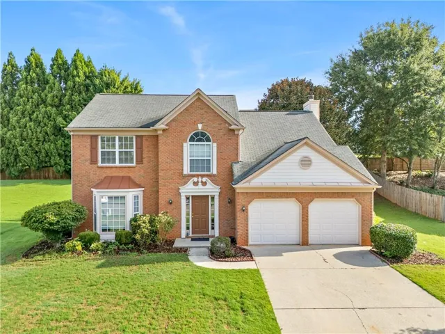 Brick-clad two-story residence featuring a two-car garage, bay window with copper awning, arched window details, and mature landscaping