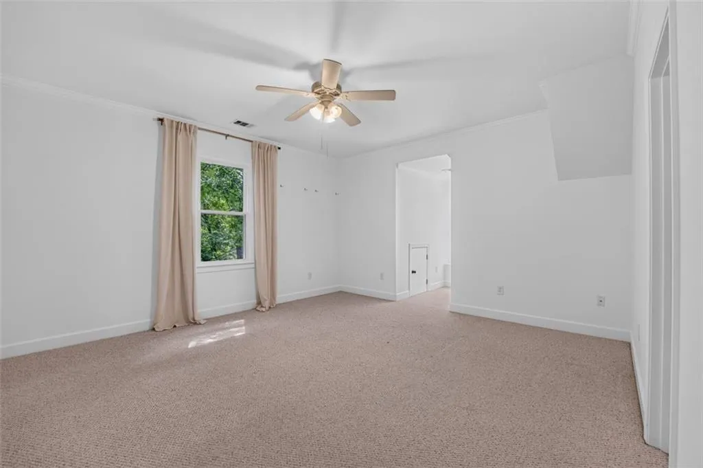 Carpeted room with white walls, a ceiling fan with integrated lighting, and crown molding