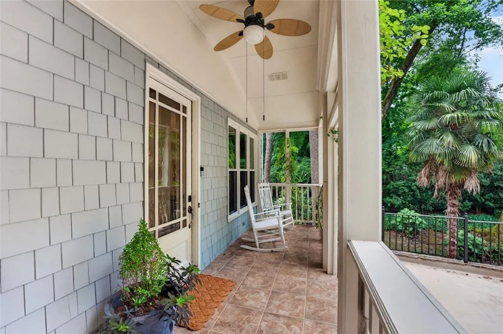 Covered porch with tile flooring, shaker-style siding, overhead ceiling fan, and surrounding natural foliage