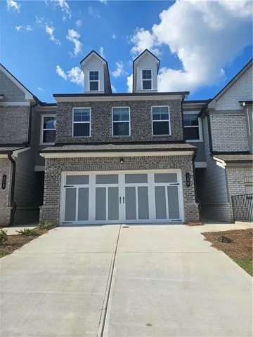 Gray brick facade with siding accents, two dormer windows, and a concrete driveway