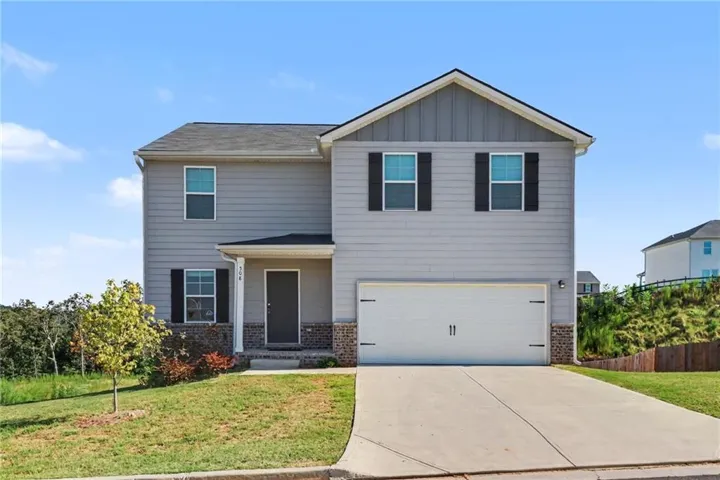 Two-story home featuring gray fiber cement siding, a welcoming front porch with brick detailing, and a two-car garage with paneled doors