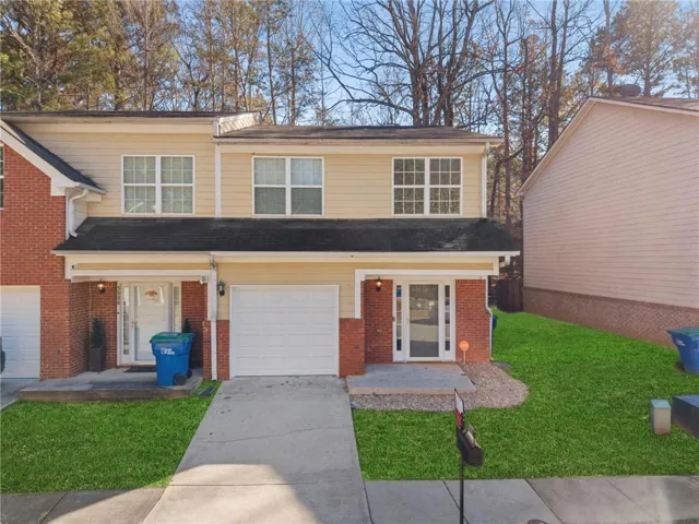 Welcoming front elevation featuring a brick and vinyl composite exterior, multi-pane double-hung windows, an attached single-car garage with white panel door, and a concrete driveway leading to the entry