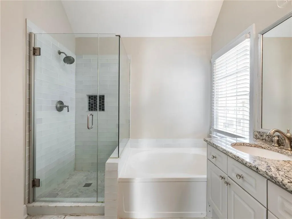 Full bathroom with healthy amount of natural light, a garden tub, a shower stall, vanity, and lofted ceiling