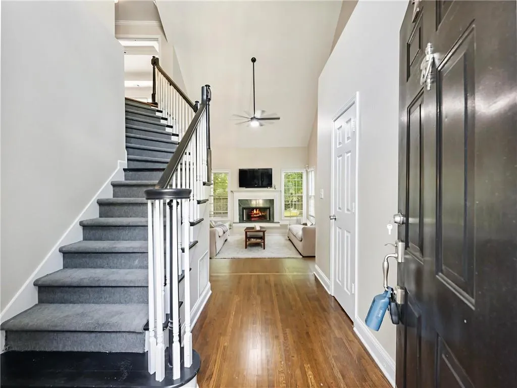 Entrance foyer with ceiling fan, a high ceiling, stairs, dark wood-type flooring, and a lit fireplace