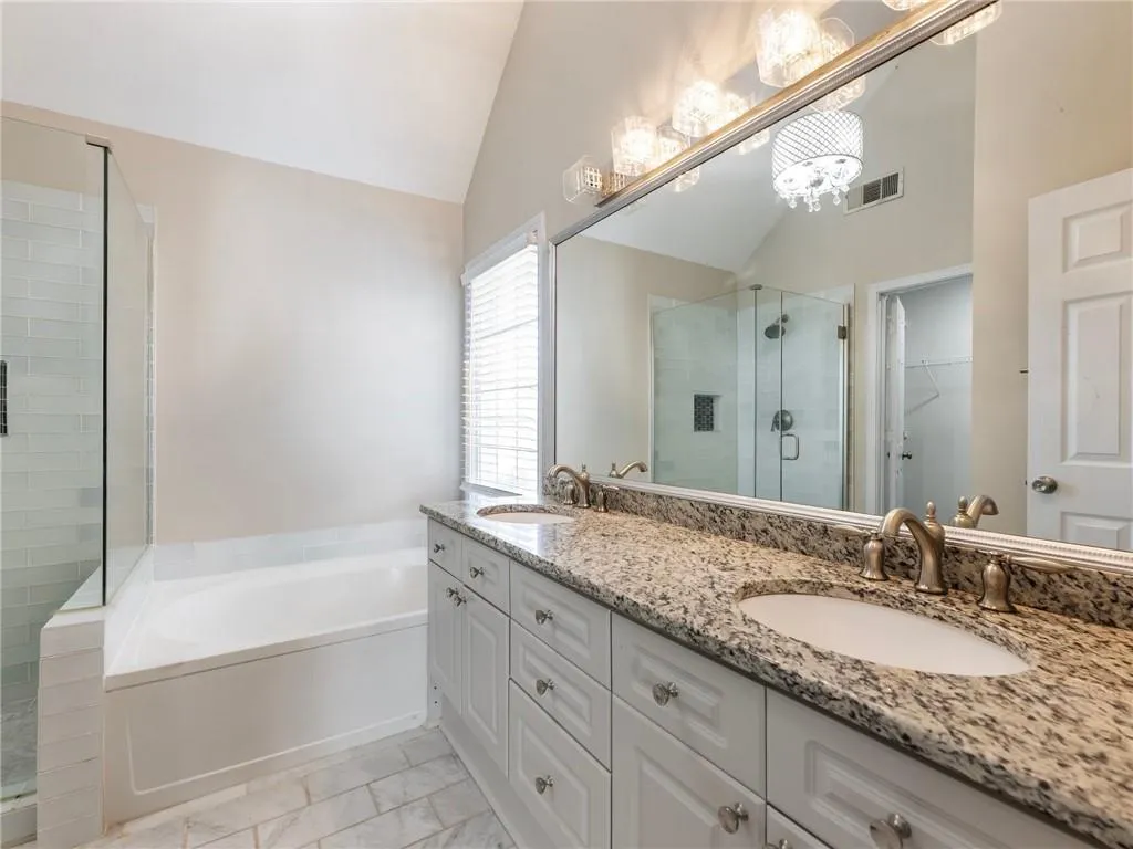 Bathroom featuring a stall shower, double vanity, a garden tub, a walk in closet, and marble look tile flooring