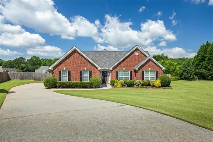 Brick exterior featuring a gabled roofline, black window shutters, a concrete driveway, and front landscaping