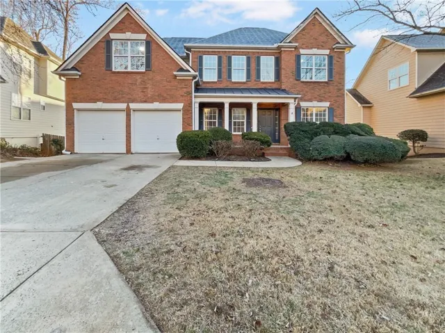 Traditional-style house with brick siding, concrete driveway, covered porch, an attached garage, and a front yard