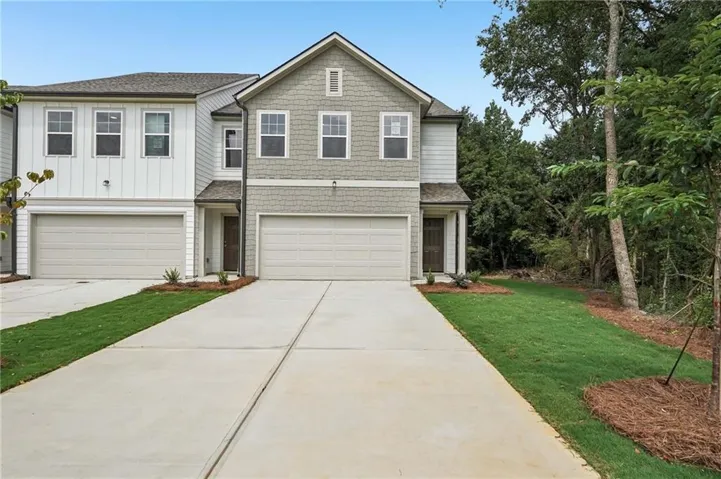 Contemporary townhome exterior featuring a combination of horizontal siding and shake siding, an attached garage, a paved driveway, and manicured front landscaping