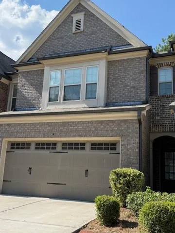 Brick exterior with a gabled roofline, featuring a two-car garage with decorative hardware, and mature landscaping