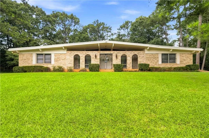 Brick exterior with arched entryways, a wide front lawn, and mature trees framing the property