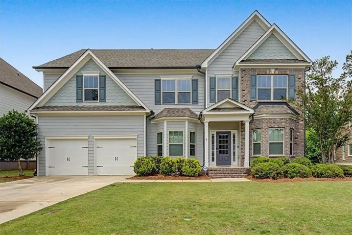 Two-story residence featuring light gray siding, brick accents, a covered front entry, a double-bay garage, and a manicured lawn with established landscaping