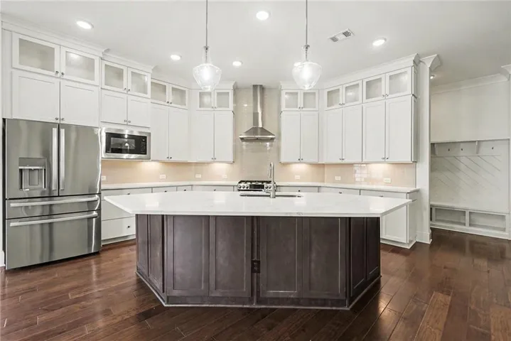 Gourmet kitchen featuring a large central island, white cabinetry with glass-front uppers, stainless steel appliances, and wood-finish flooring