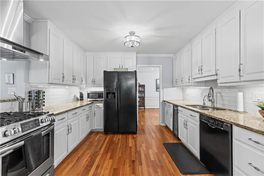 Kitchen with black appliances, wall chimney range hood, a sink, and white cabinets