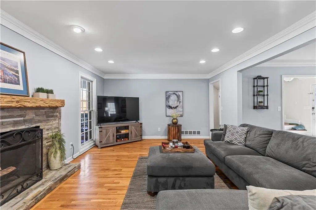 Living room with baseboards, light wood-style flooring, ornamental molding, a stone fireplace, and recessed lighting