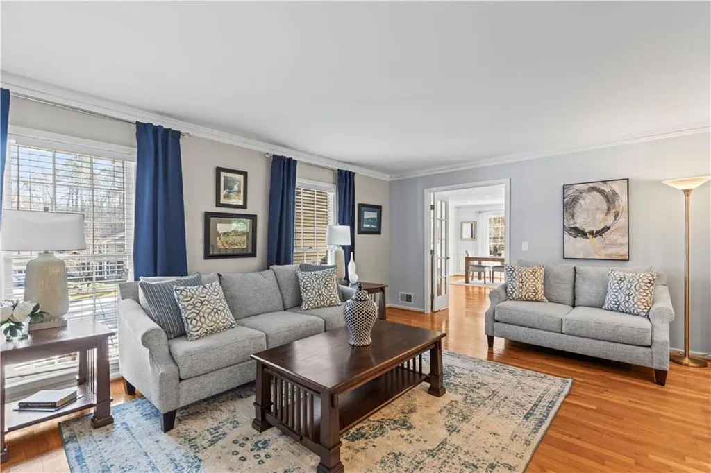 Living area featuring ornamental molding, light wood finished floors, visible vents, and baseboards