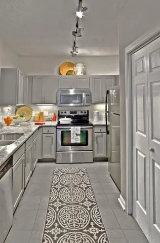 Kitchen featuring appliances with stainless steel finishes, rail lighting, gray cabinets, and light tile floors