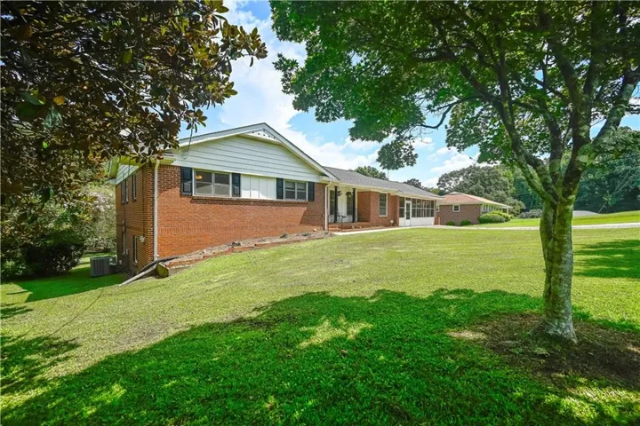 Brick exterior, white siding accents, mature trees, manicured lawn, and an enclosed porch