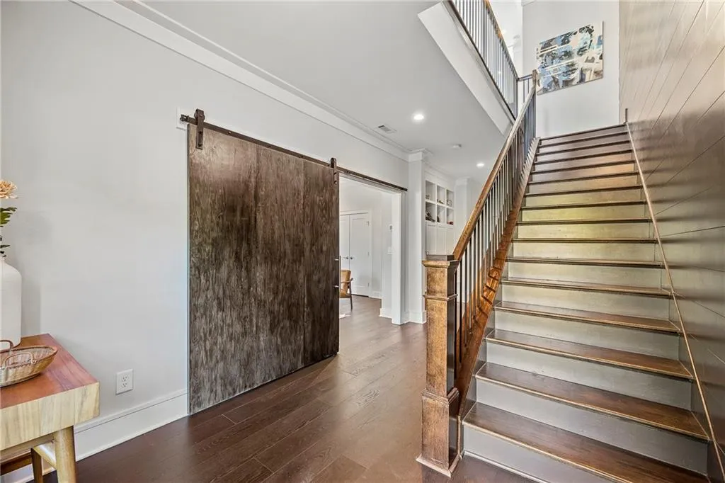 Staircase with a barn door, wood finished floors, recessed lighting, and ornamental molding