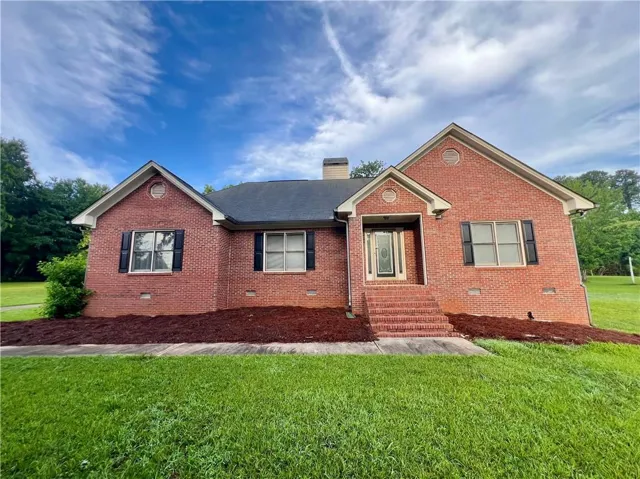 Brick exterior with a dark shingle roof, contrasting black window shutters, and a prominent front entrance with brick steps