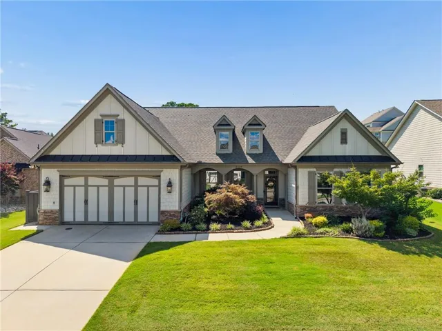 Craftsman-style exterior featuring a multi-gable roofline, stacked stone accents, decorative garage doors, a covered entry porch, and a manicured front lawn with mature landscaping