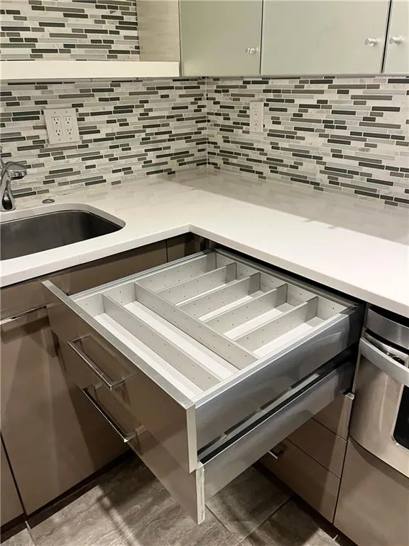 Kitchen view of a warming drawer, backsplash, and light stone counters