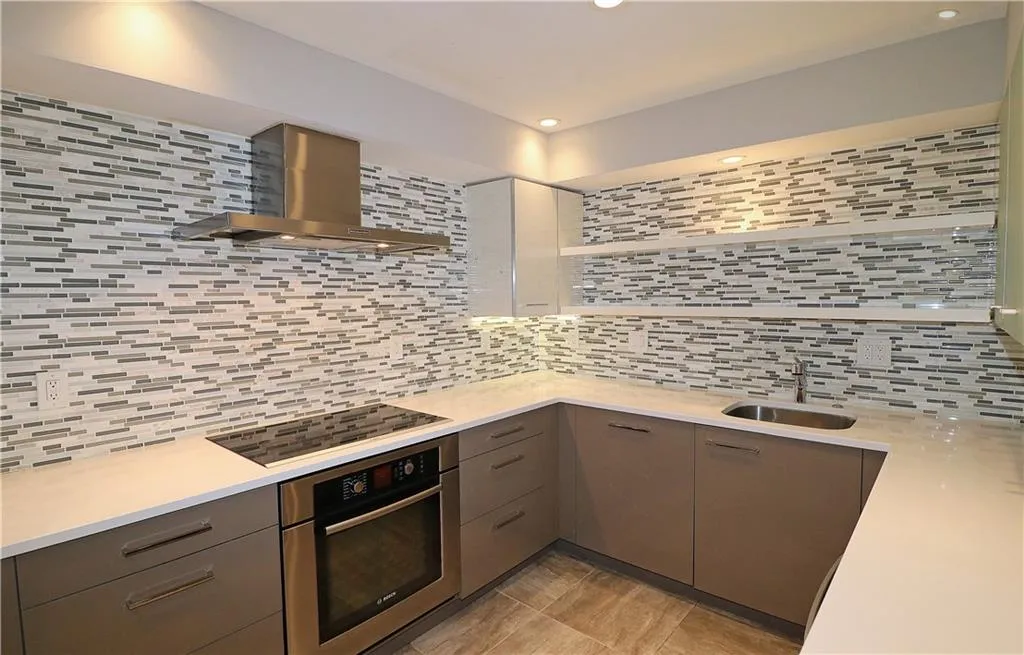 Kitchen with oven, wall chimney range hood, black electric stovetop, tasteful backsplash, and gray cabinetry