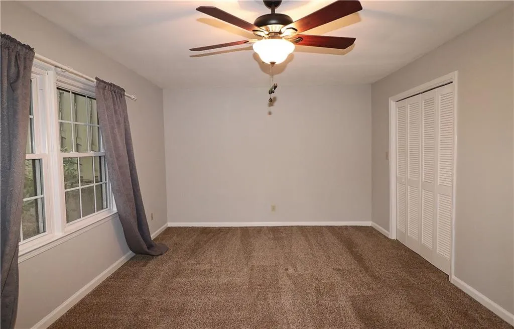 Unfurnished bedroom featuring dark colored carpet, a closet, and a ceiling fan