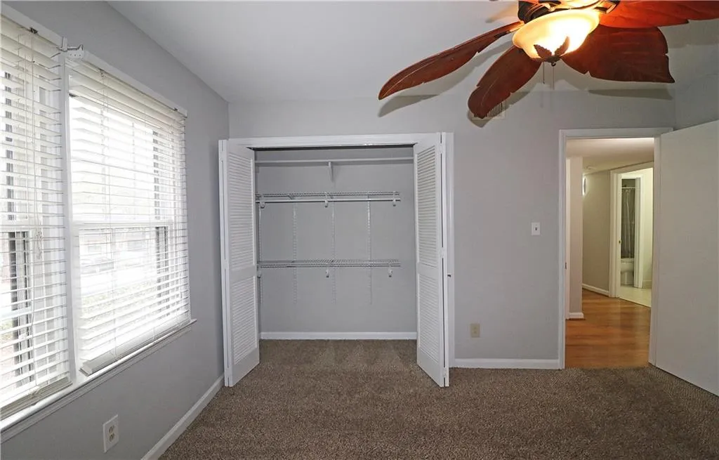 Unfurnished bedroom with a ceiling fan, dark colored carpet, and a closet