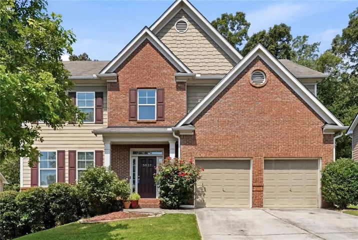 Traditional two-story residence featuring a brick and siding exterior, a two-car garage, established front landscaping, and a covered entry