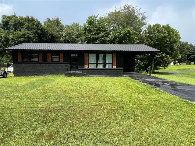 Black exterior with a metal roof, wood-finish shutters, and an attached carport