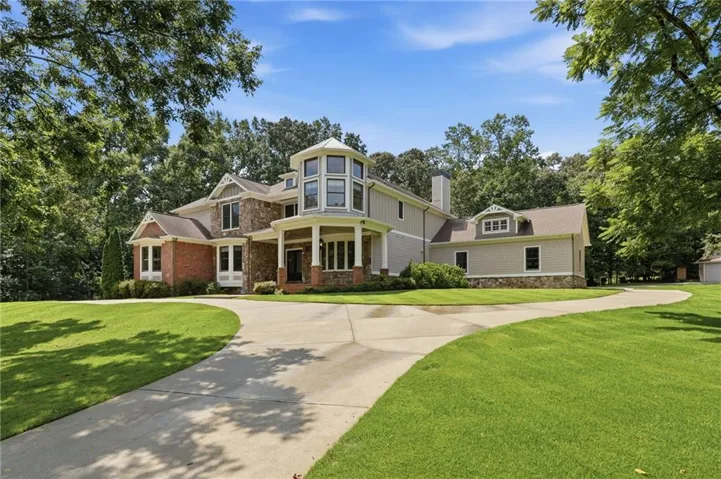 Striking two-story Colonial residence featuring a circular turret with multi-pane windows, brick and vinyl exterior, arched entryway with sidelights, and a curved driveway