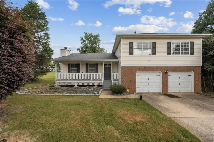 Split-level residence featuring a covered front porch with white railing, two-car garage, brick facade, and light-colored siding