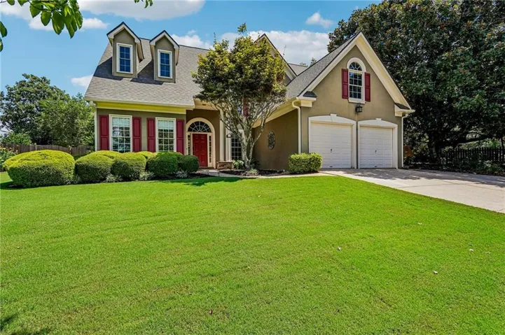Dormer windows, red entry door, two-car garage, and manicured landscaping