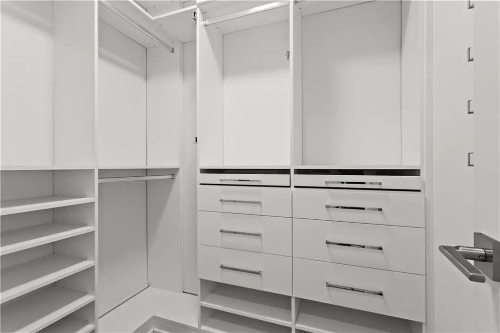 Built-in closet system featuring white cabinetry, multiple shelving units, integrated hanging rods, and sleek drawer storage with polished chrome hardware