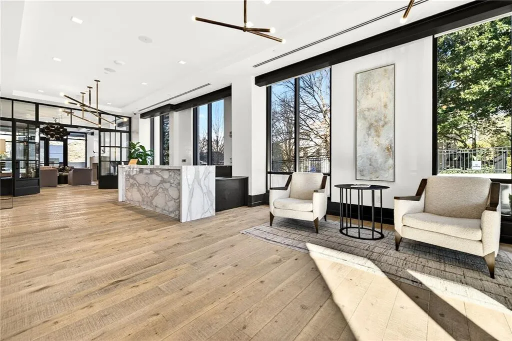 Spacious interior featuring wood-finish flooring, a white marble-patterned reception desk, black-framed windows, and a modern linear chandelier