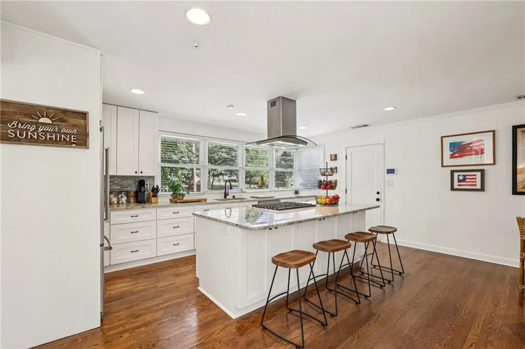 Kitchen with light stone counters, a breakfast bar area, white cabinets, a center island, and dark wood-style flooring