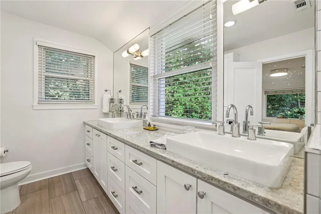 Full bath with healthy amount of natural light, double vanity, lofted ceiling, a chandelier, and wood tiled floors