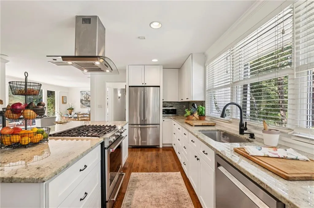 Kitchen with light stone countertops, stainless steel appliances, island range hood, recessed lighting, and dark wood-type flooring