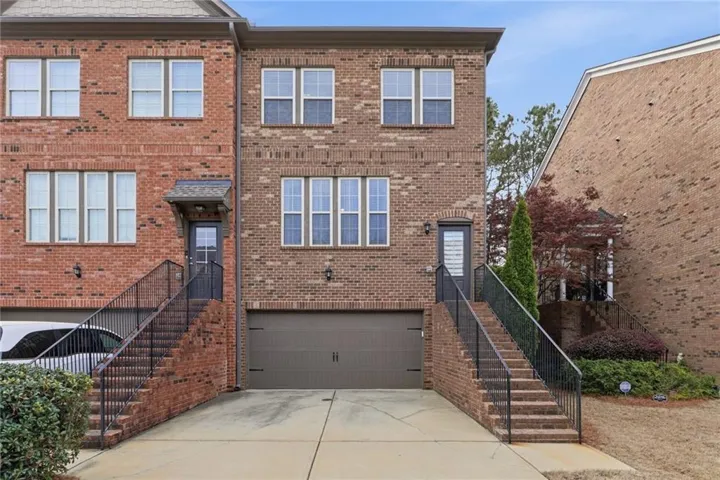 Brick façade townhome featuring a private garage, exterior sconce lighting, and a prominent front entry with a covered awning