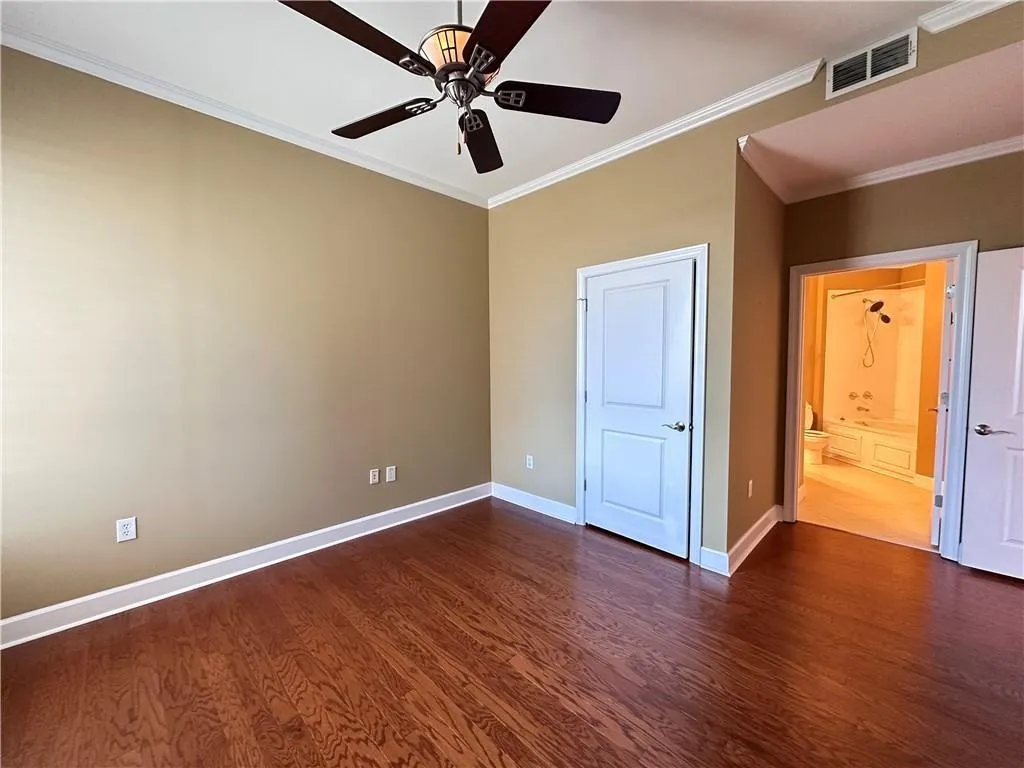 Unfurnished bedroom featuring ornamental molding, dark wood-style flooring, a ceiling fan, and connected bathroom