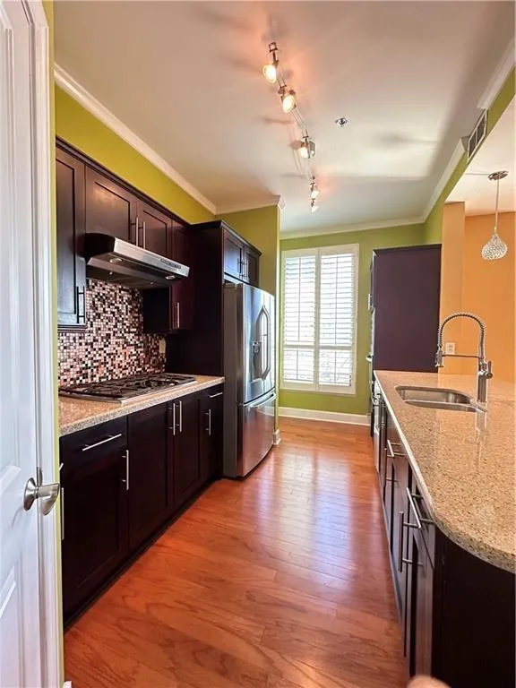 Kitchen with crown molding, light stone counters, light wood-type flooring, stainless steel appliances, and dark wood finish cabinets