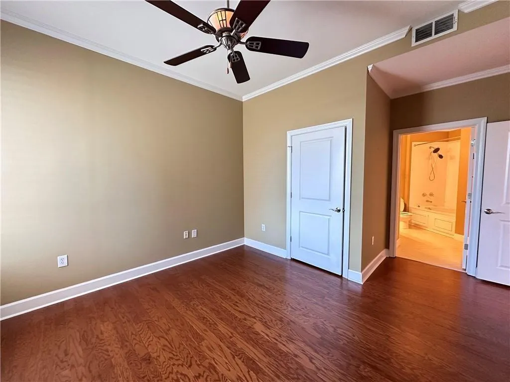 Unfurnished bedroom with ornamental molding, ceiling fan, dark wood-type flooring, and connected bathroom