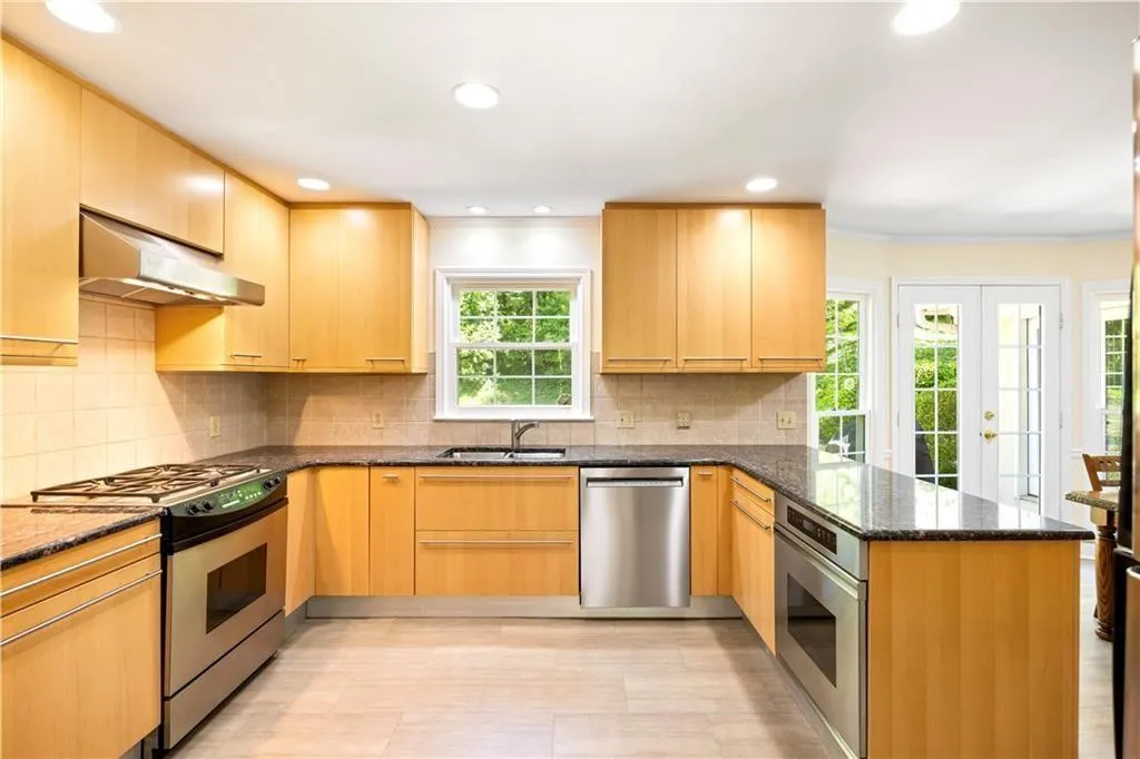 Kitchen featuring under cabinet range hood, stainless steel appliances, a sink, dark stone counters, and a peninsula
