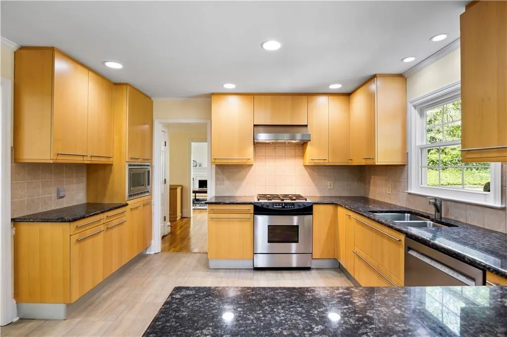 Kitchen with stainless steel appliances, a sink, dark stone counters, exhaust hood, and ornamental molding