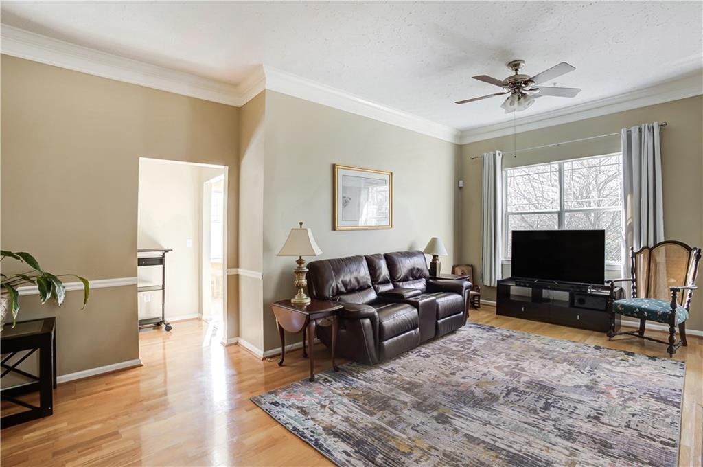 Living room with ornamental molding, a textured ceiling, ceiling fan, and light hardwood / wood-style flooring