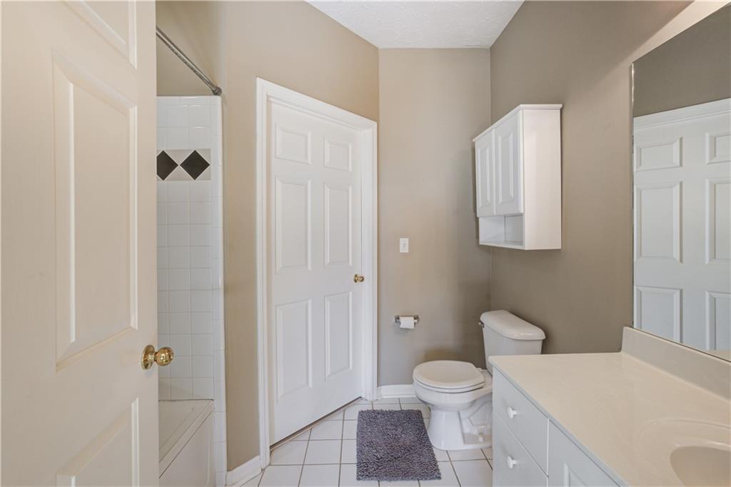 Full bathroom featuring tiled shower / bath combo, toilet, vanity with extensive cabinet space, and tile flooring