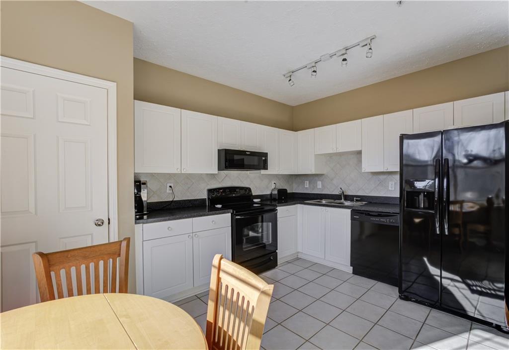 Kitchen featuring light tile floors, white cabinets, rail lighting, black appliances, and backsplash