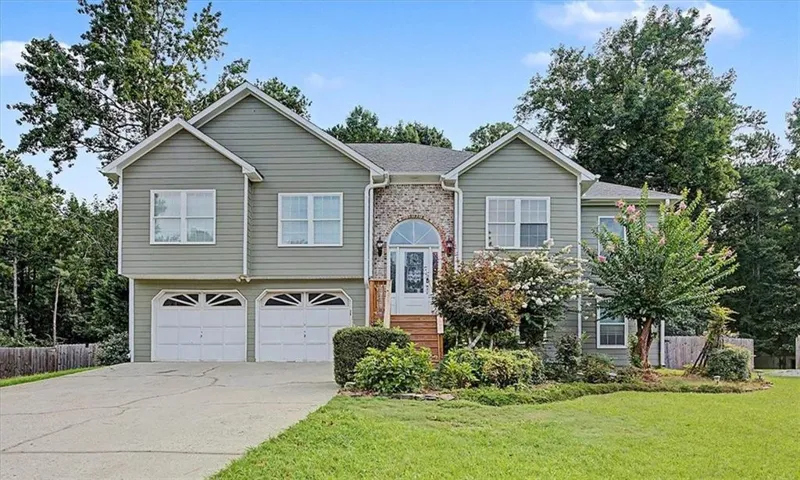Exterior featuring light green siding, stone accents, two-car garage, front entry with arched transom, and established landscaping