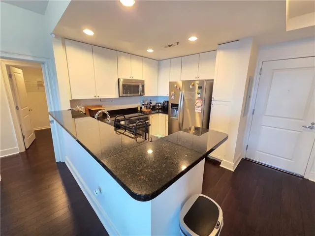 Kitchen featuring dark wood-finish flooring, white cabinetry, dark stone countertops, stainless steel appliances, and recessed lighting